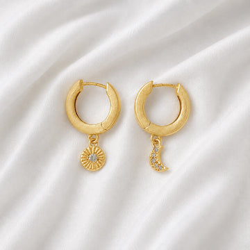 Silver_hoop_earrings_in_gold_plated_silver_with_sun_and_moon_charms_at_front_angle_view_on_soft_fabric_background