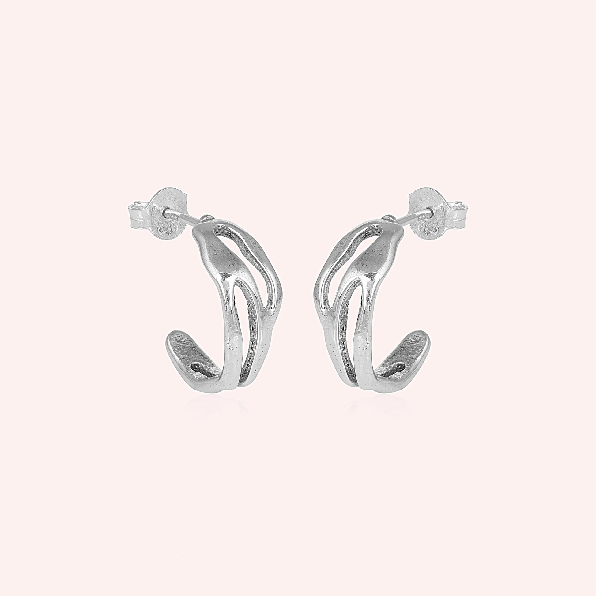 Silver hoop earrings shown at side angled view featuring sculpted open hoop design in polished silver on soft pink background