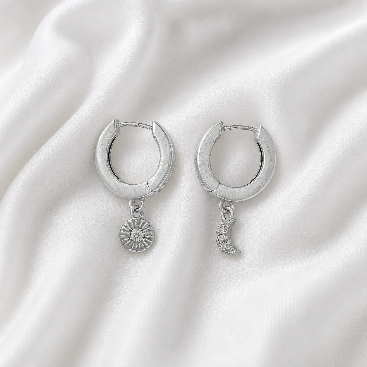 Silver_hoop_earrings_in_sterling_silver_with_sun_and_moon_charms_at_front_angle_view_on_soft_fabric_background