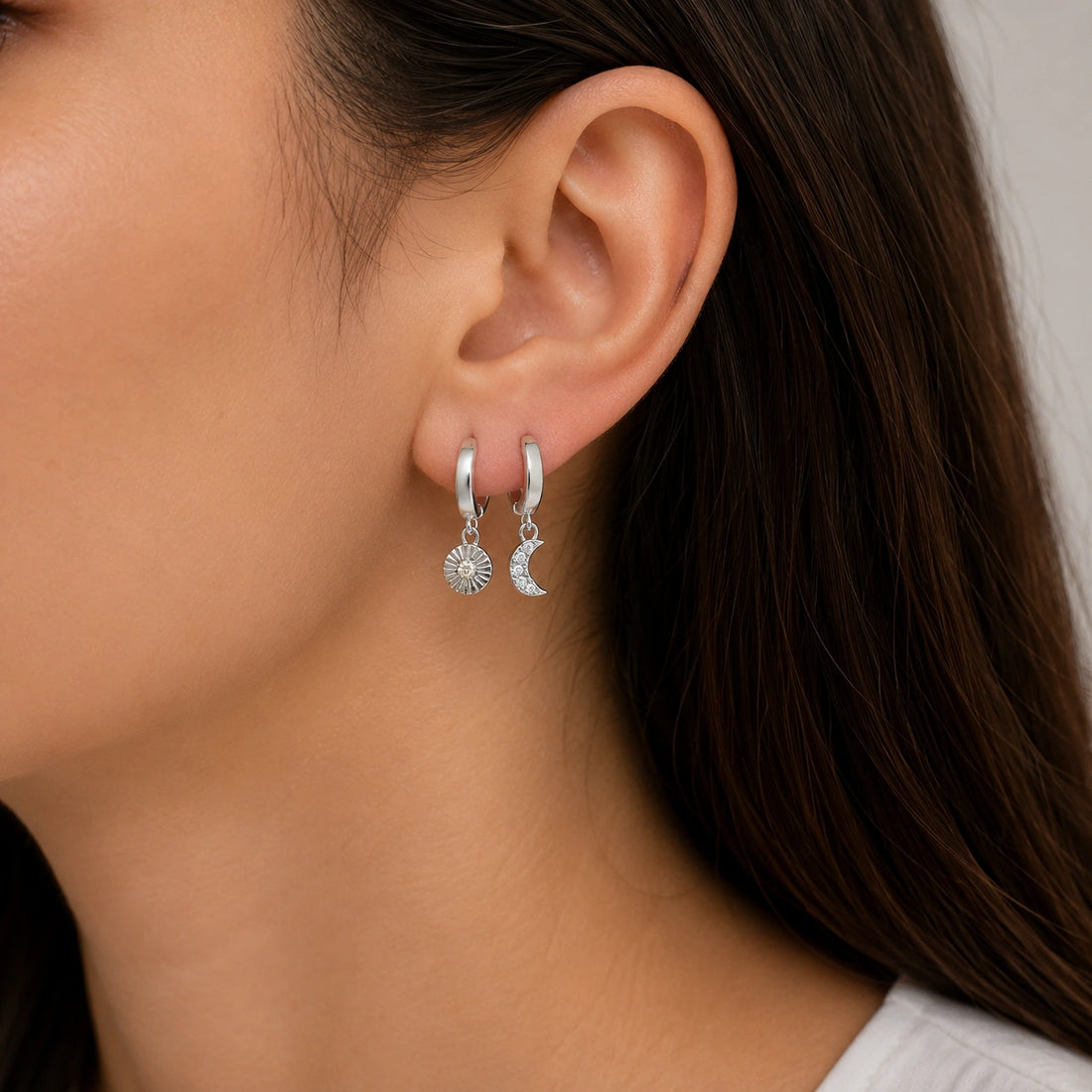 Silver_hoop_earrings_in_gold_plated_silver_with_sun_and_moon_charms_at_front_angle_view_on_soft_fabric_background