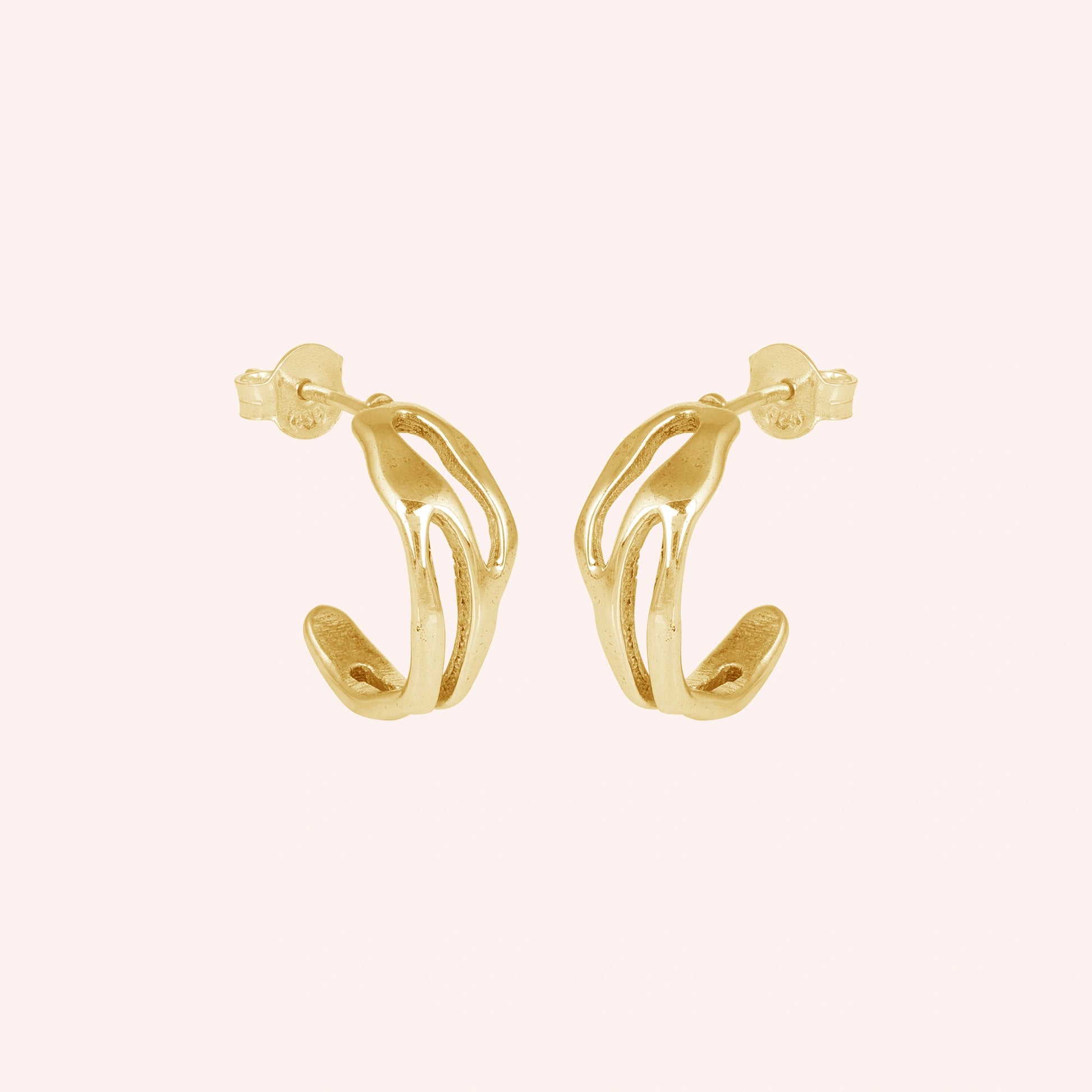 gold plated hoop earrings shown at side angled view featuring sculpted open hoop design in gold finish on soft pink background