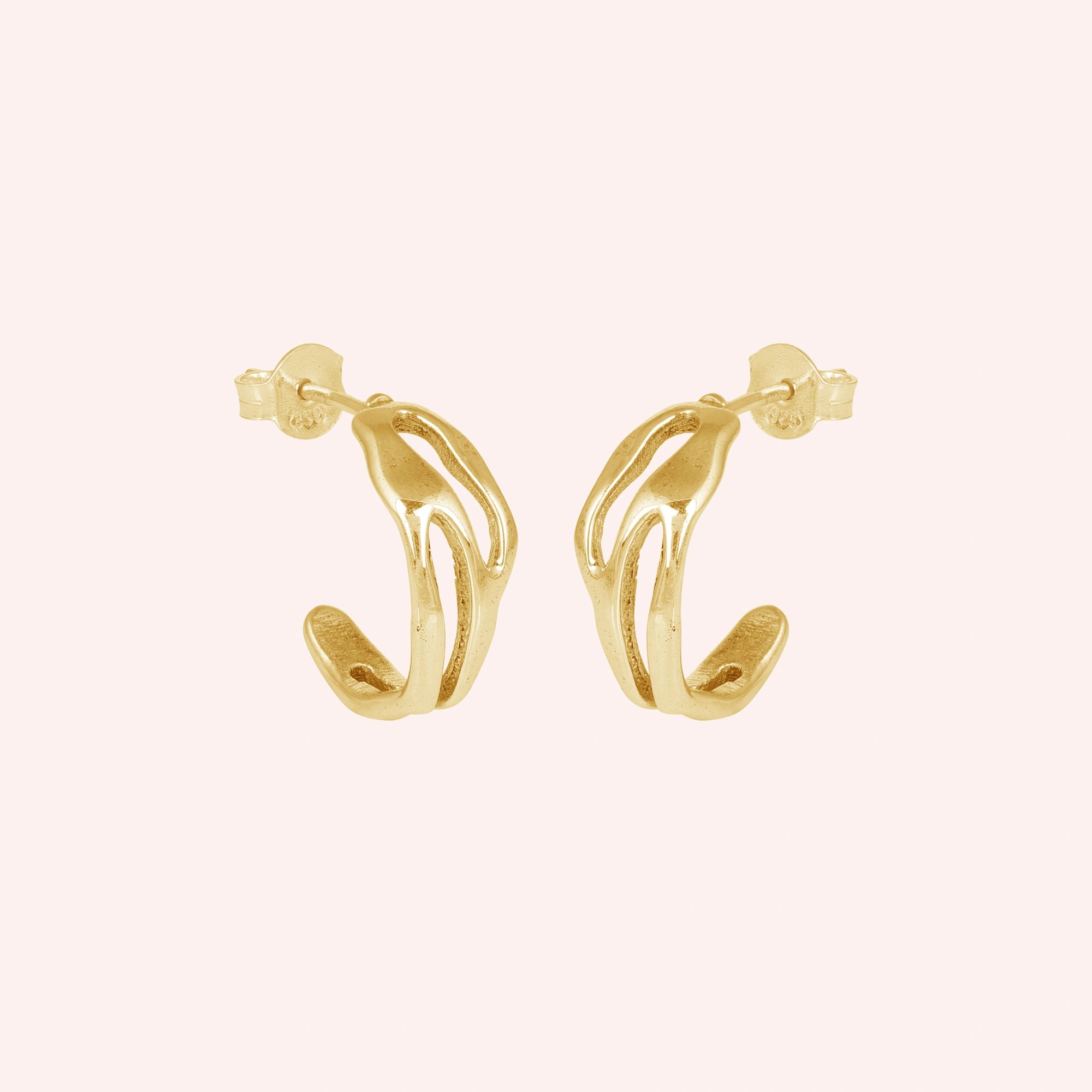 gold plated hoop earrings shown at side angled view featuring sculpted open hoop design in gold finish on soft pink background