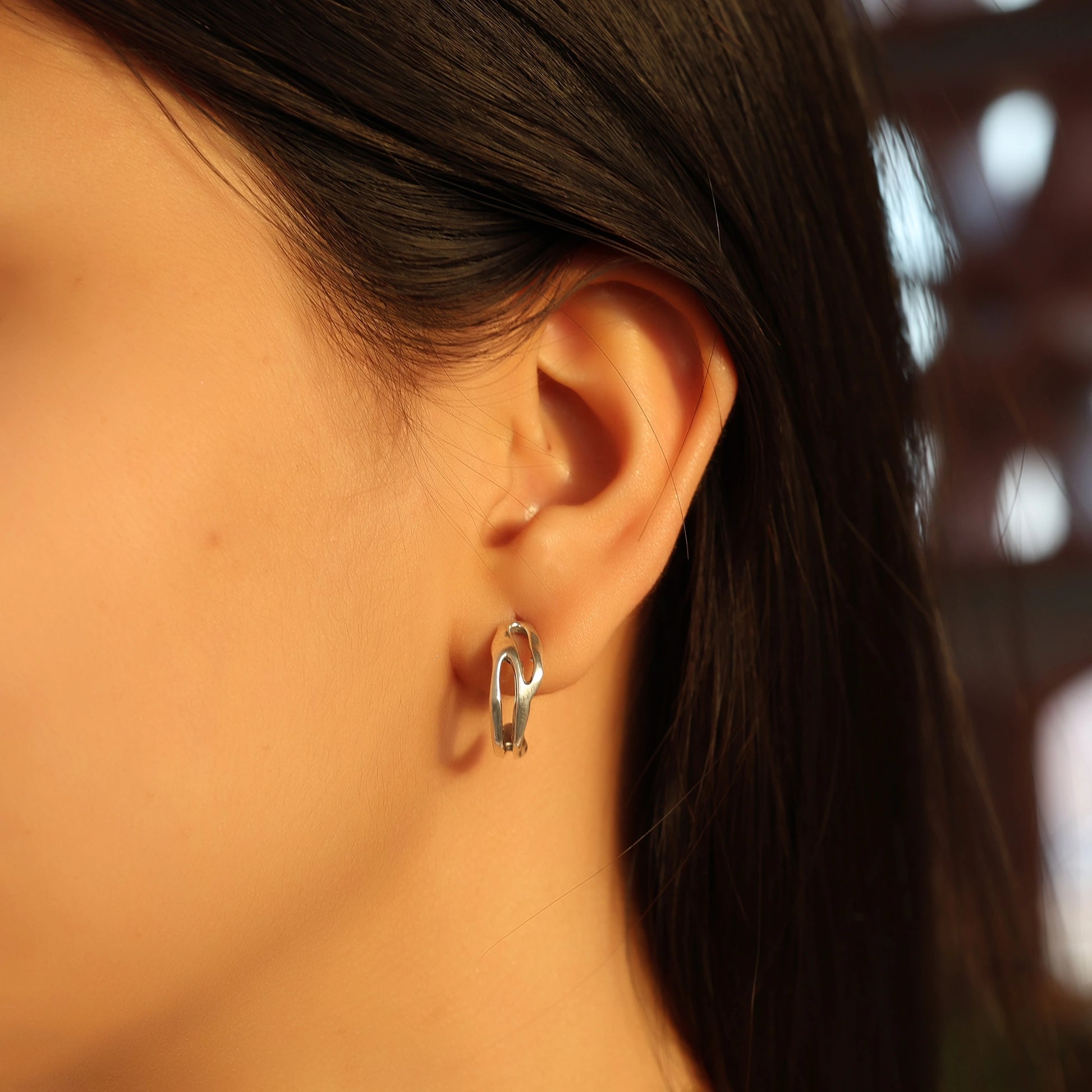 Silver hoop earrings shown at side angled view worn on ear featuring sculpted open hoop design with soft indoor background
