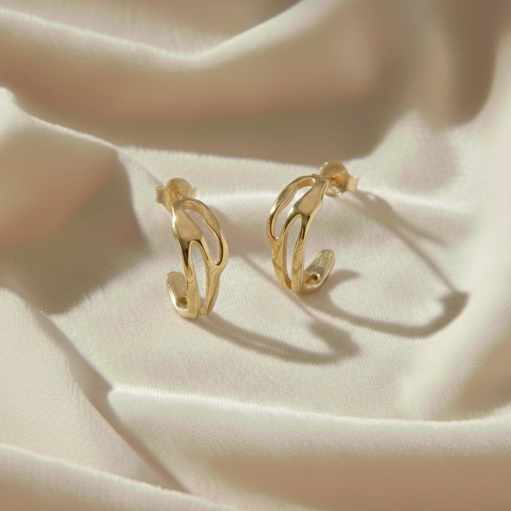 gold plated hoop earrings shown at front angled view featuring sculpted open hoop design resting on soft fabric background