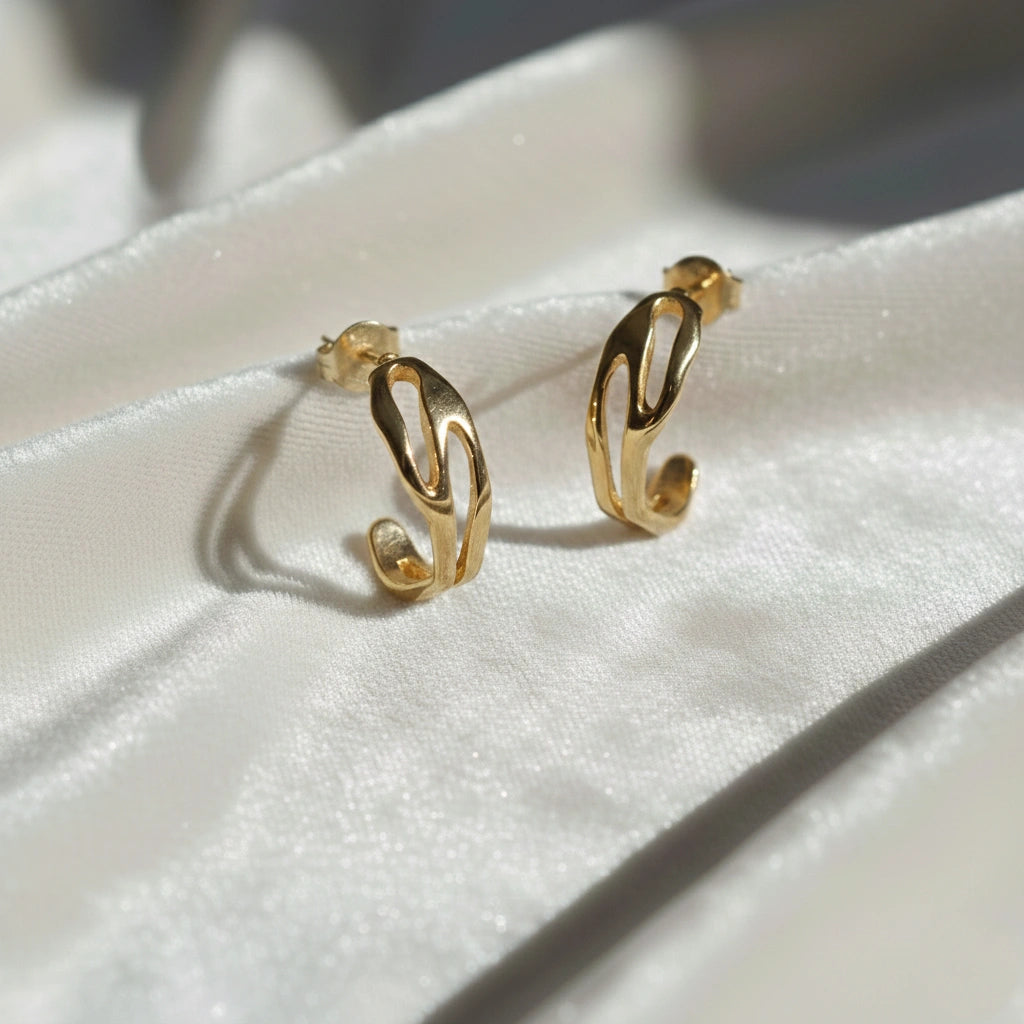 gold plated hoop earrings shown at front angled view featuring sculpted open hoop design on soft fabric background