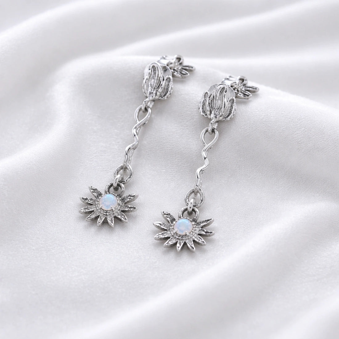 a close up high angle shot of moonstone earrings and flower earrings in silver on a soft cream fabric with wavy textures