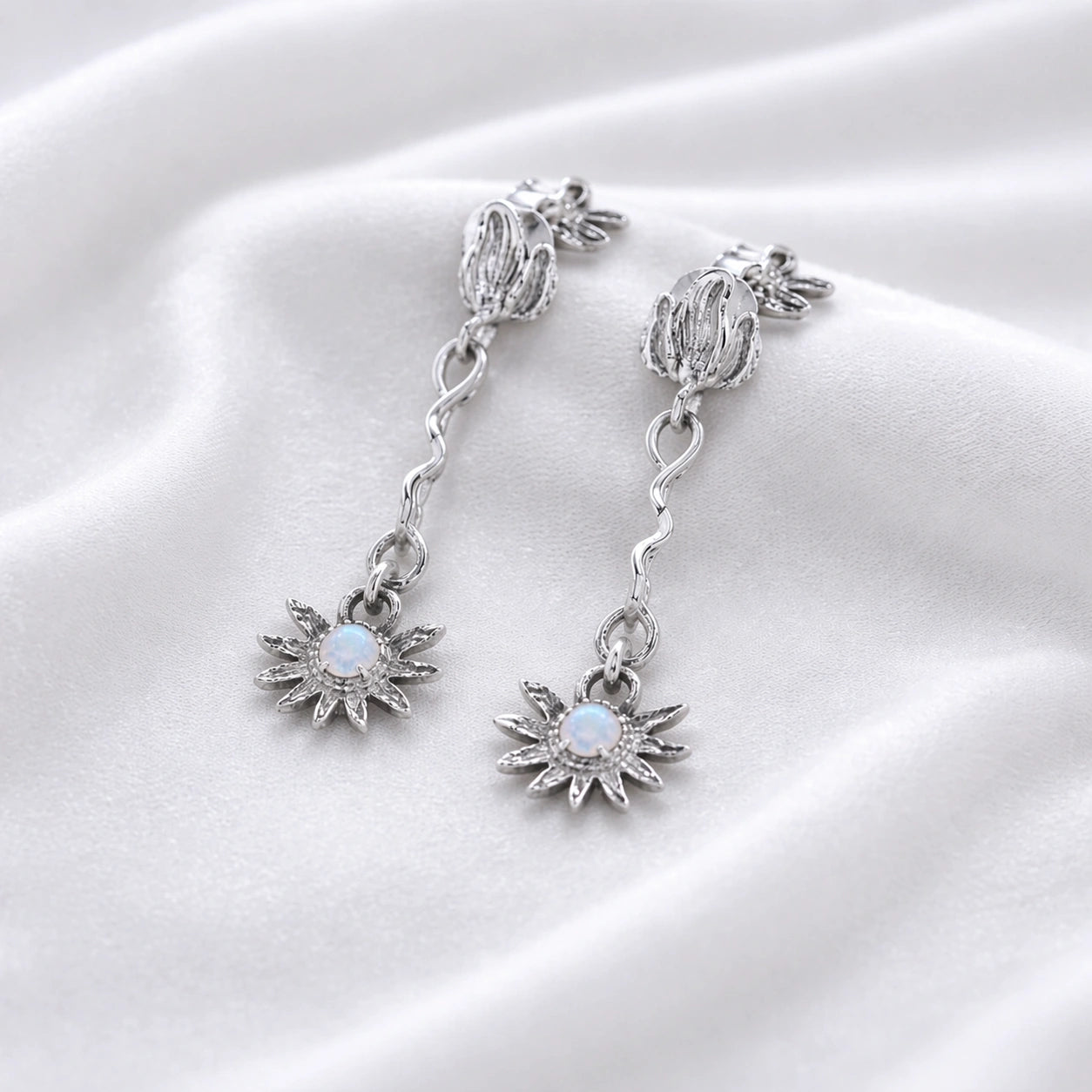 a close up high angle shot of moonstone earrings and flower earrings in silver on a soft cream fabric with wavy textures