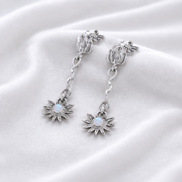a close up high angle shot of moonstone earrings and flower earrings in silver on a soft cream fabric with wavy textures
