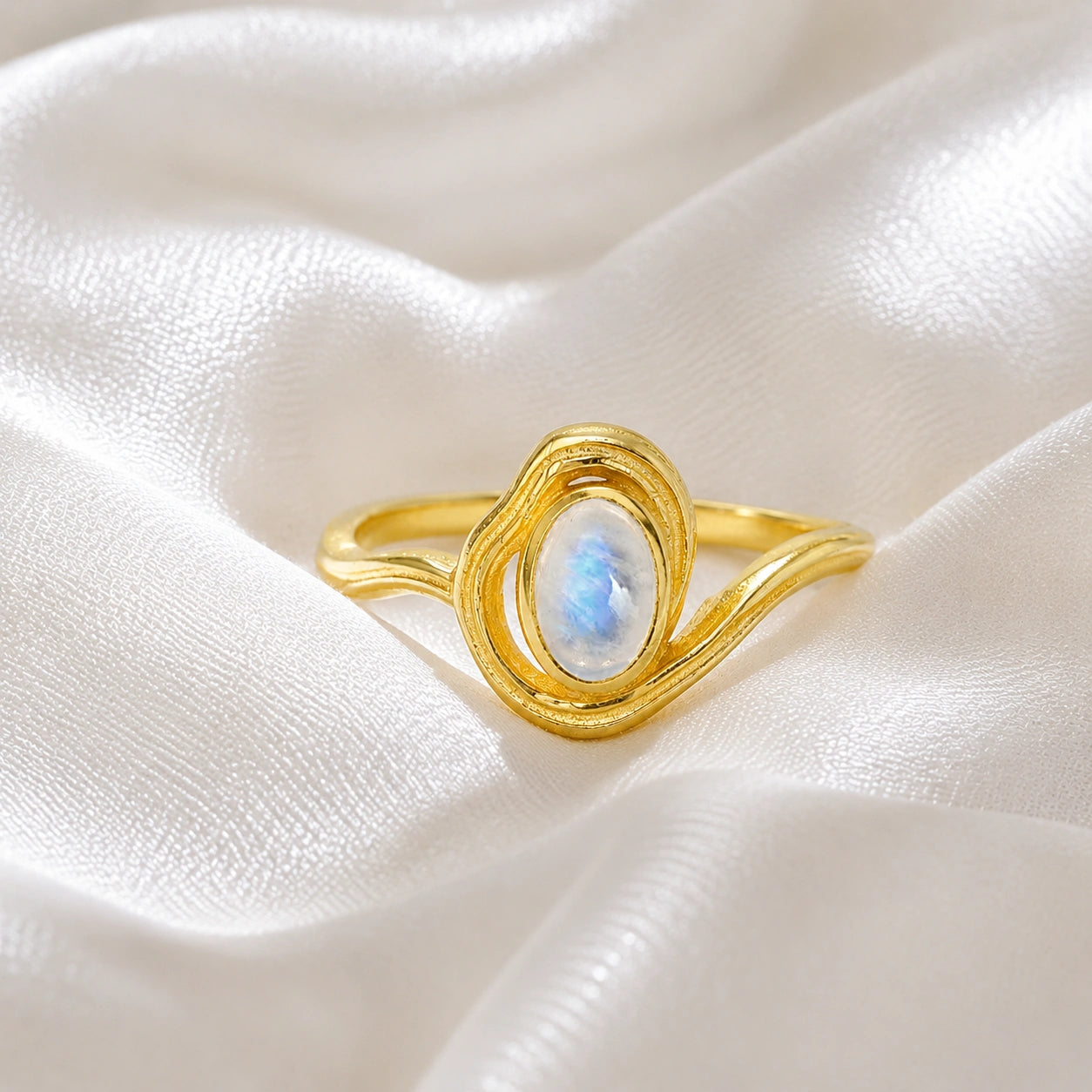 Moonstone_ring_with_gold_plated_silver_wave_band_at_front_angle_on_soft_fabric_background