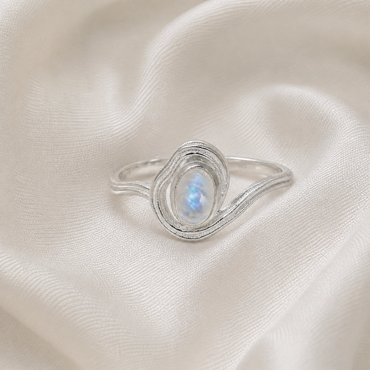 Moonstone_ring_with_sterling_silver_wave_band_at_front_angle_on_soft_fabric_background