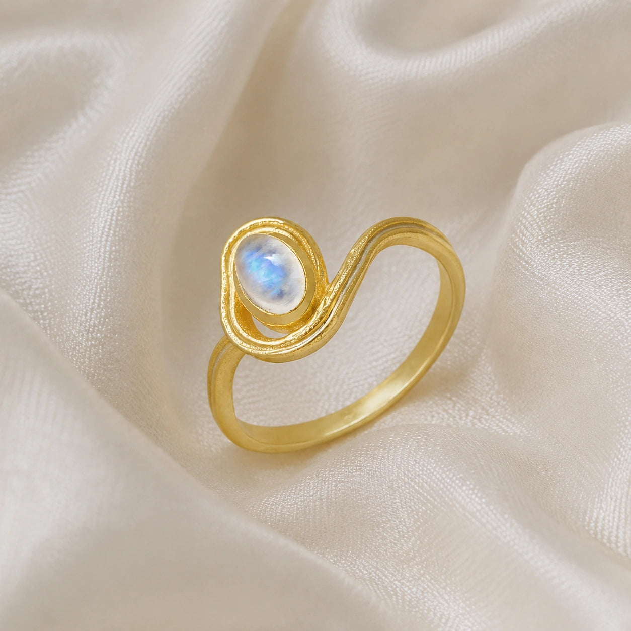 Moonstone_ring_with_gold_plated_silver_wave_band_at_side_angle_on_soft_fabric_background