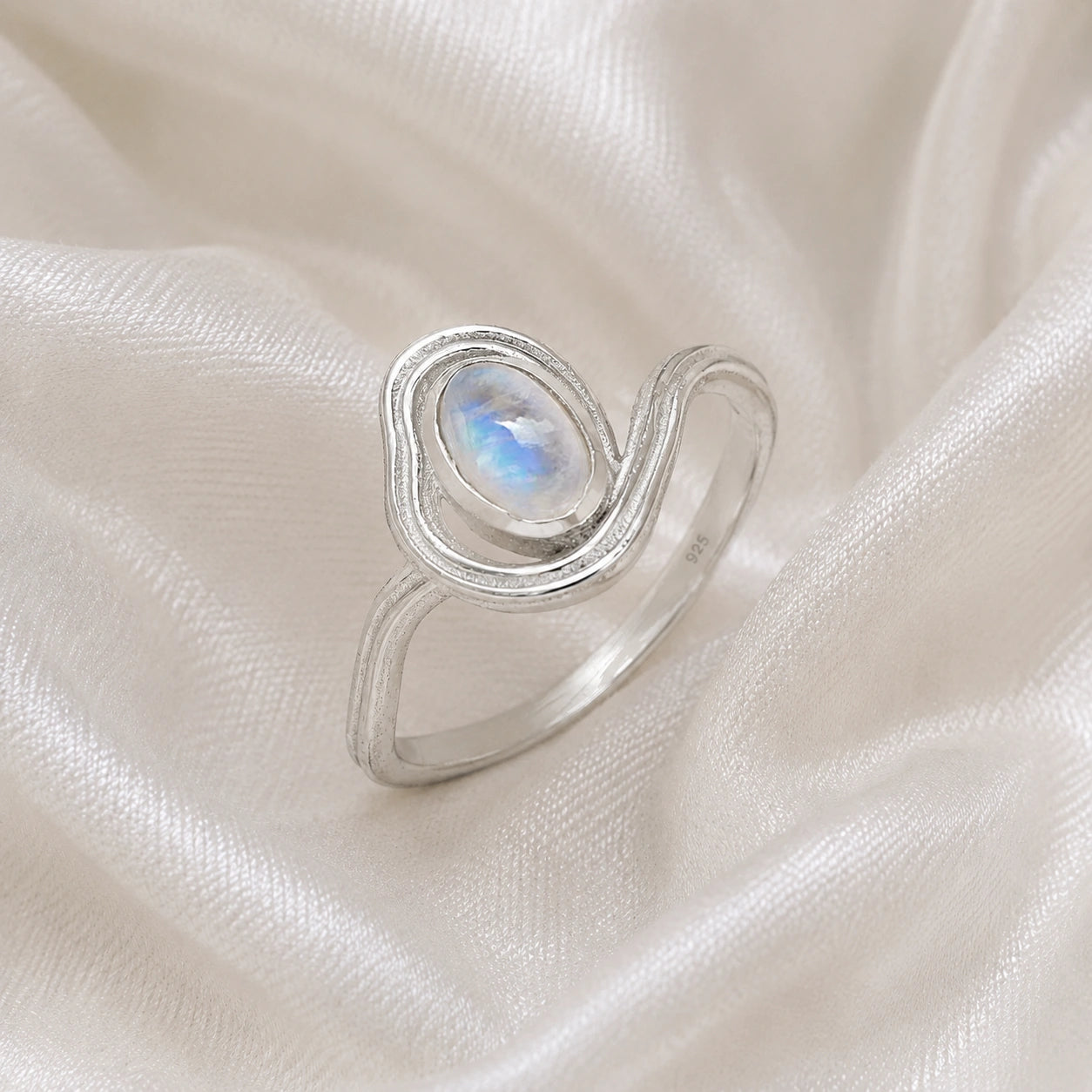 Moonstone_ring_with_sterling_silver_wave_band_at_side_angle_on_soft_fabric_background