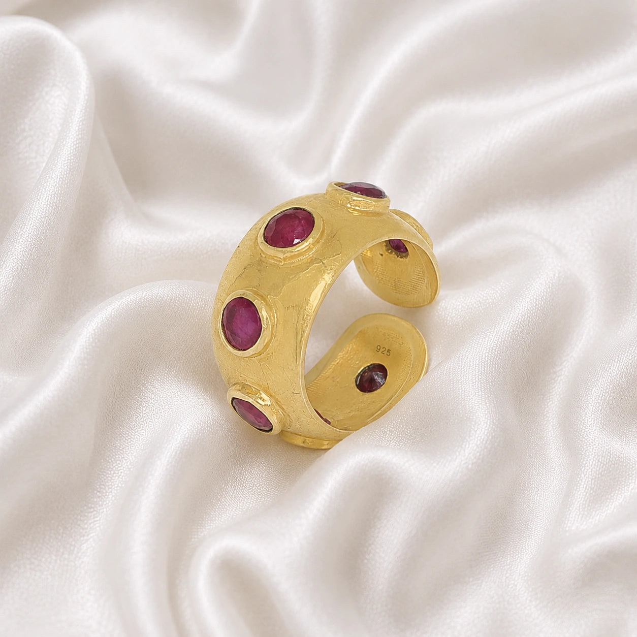 Silver_ruby_ring_in_gold_plated_silver_with_bezel_set_ruby_stones_at_slight_view_on_soft_fabric_background