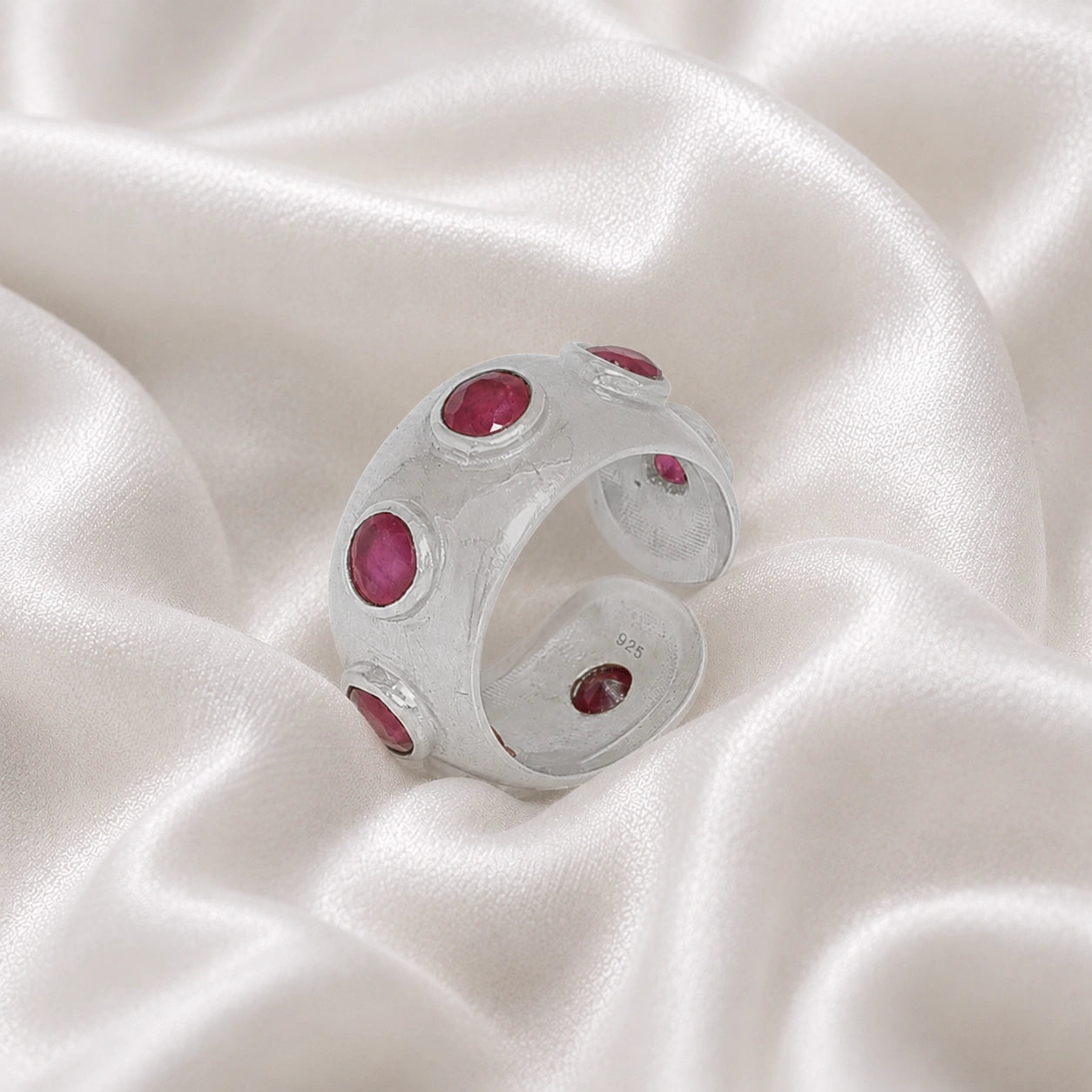 Silver_ruby_ring_in_sterling_silver_with_bezel_set_ruby_stones_at_slight_view_on_soft_fabric_background