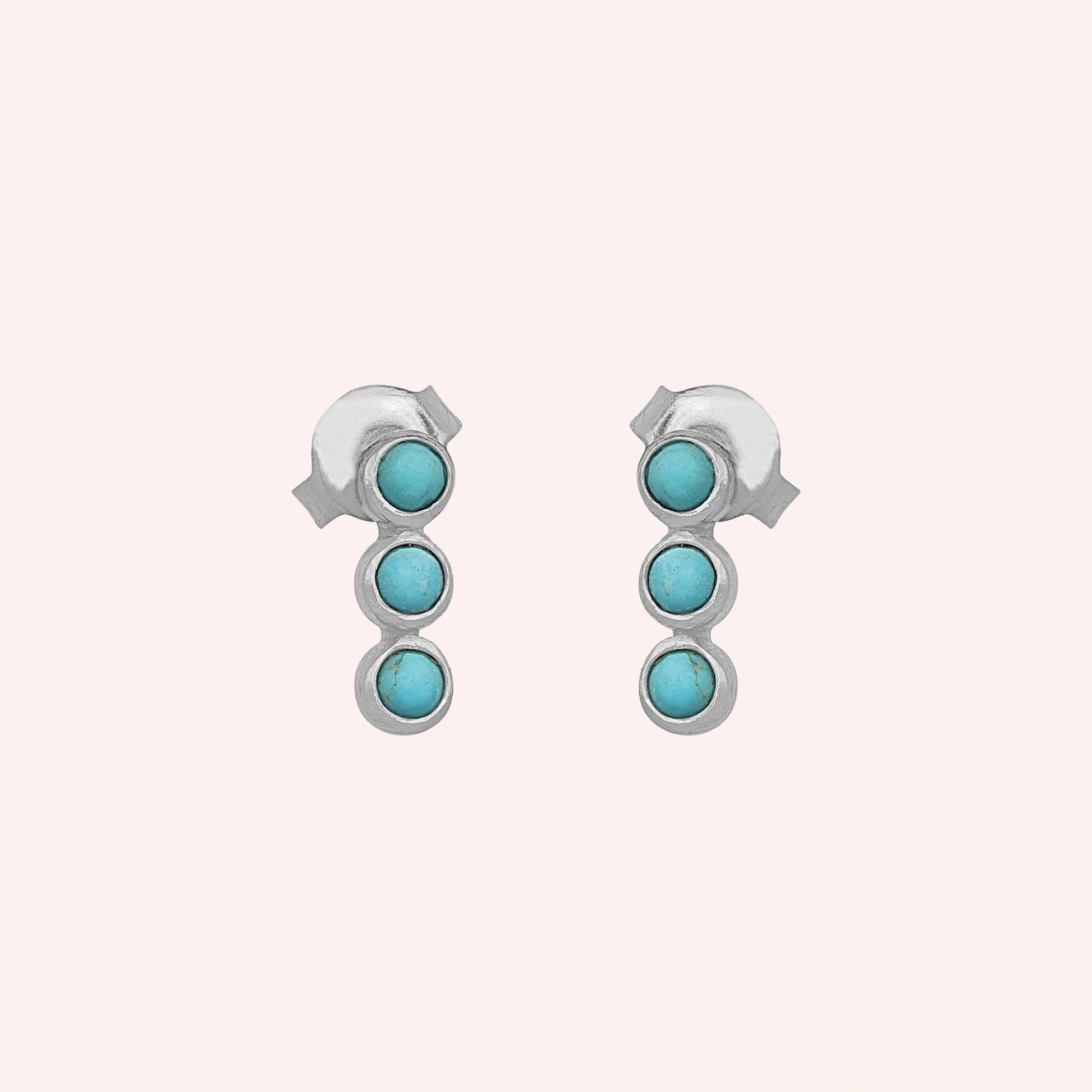 A front angle shot of these silver stud earrings with turquoise earrings stones centered on a plain light pink background