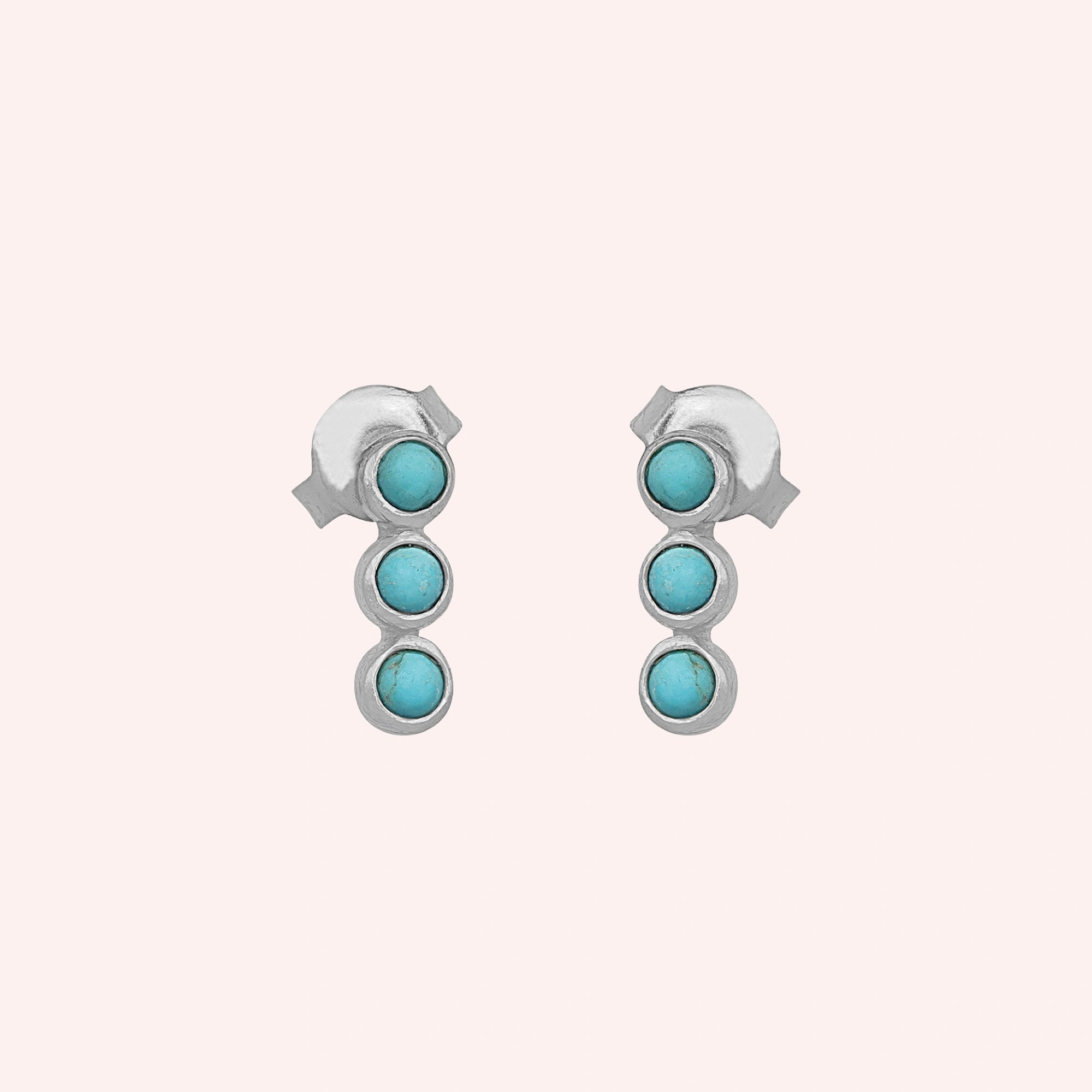 A front angle shot of these silver stud earrings with turquoise earrings stones centered on a plain light pink background