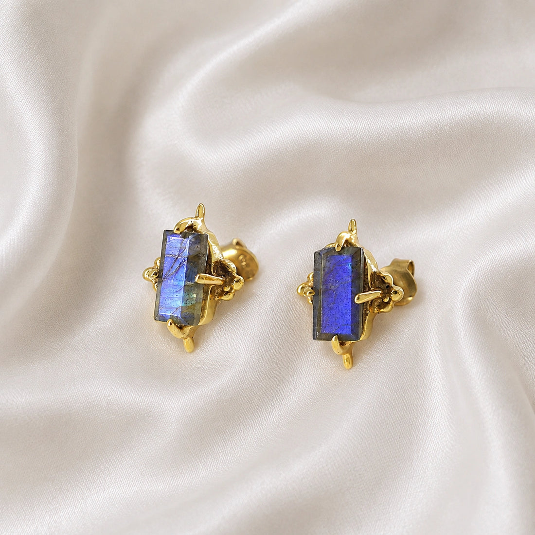 Silver_stud_earrings_in_gold_plated_silver_with_baguette_labradorite_stone_at_front_angle_view_on_soft_fabric_background