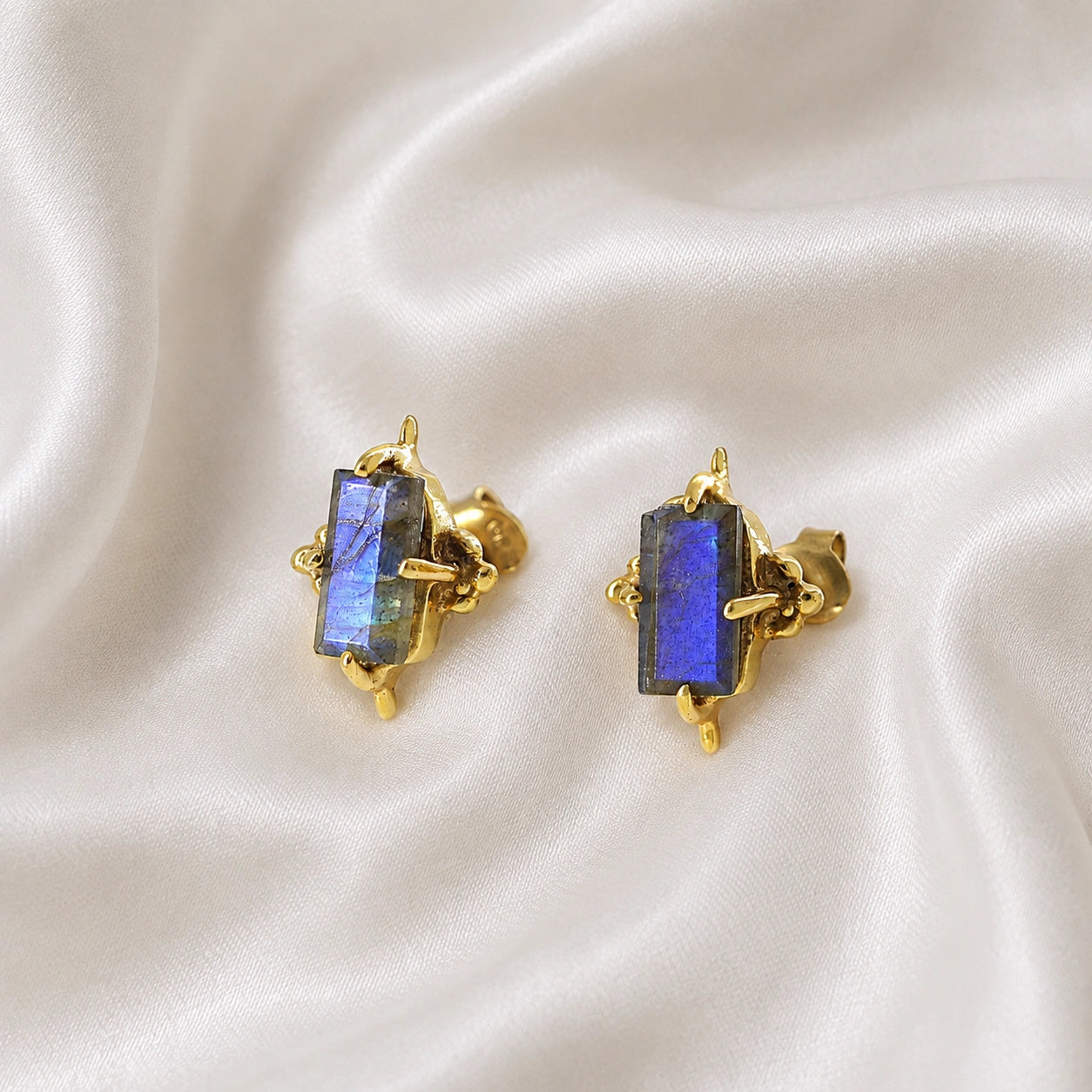 Silver_stud_earrings_in_gold_plated_silver_with_baguette_labradorite_stone_at_front_angle_view_on_soft_fabric_background