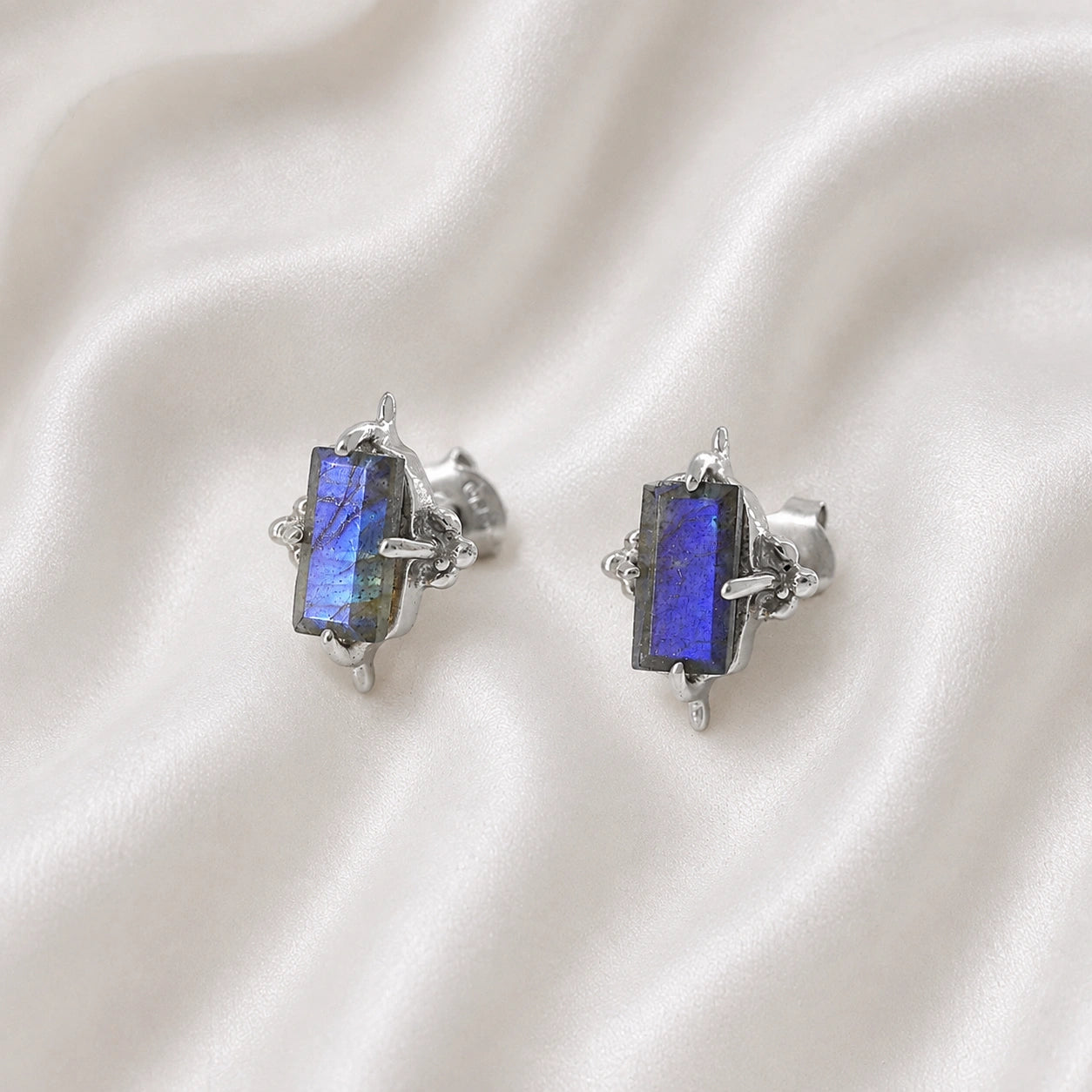 Silver_stud_earrings_in_sterling_silver_with_baguette_labradorite_stone_at_front_angle_view_on_soft_fabric_background