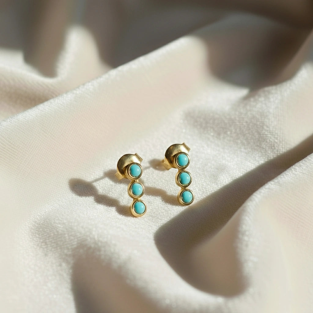 Gold plated silver stud earrings with turquoise earrings stones set in a vertical row at a staright angle on white velvet cloth