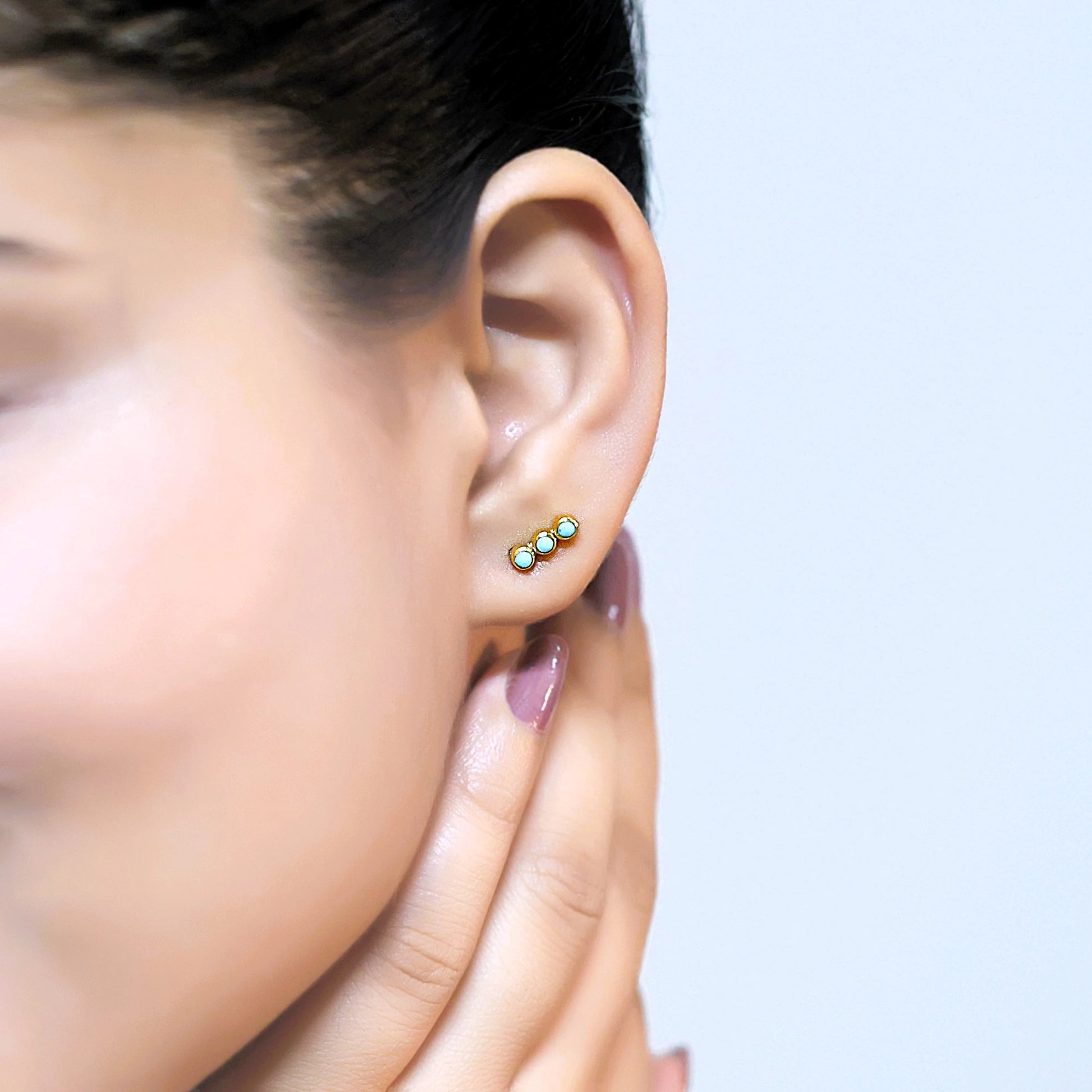 Gold plated silver stud earrings with turquoise earrings stones worn by a model at a side angle