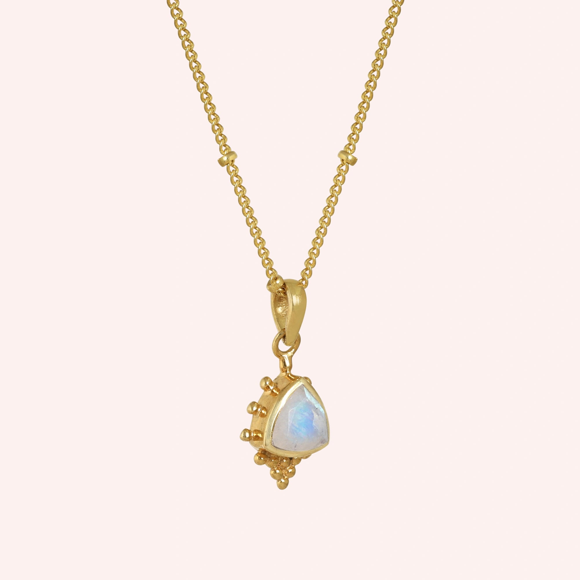 Simple_necklace_with_triangular_moonstone_pendant_gold_plated_silver_at_slightly_angled_on_solid_pink_background