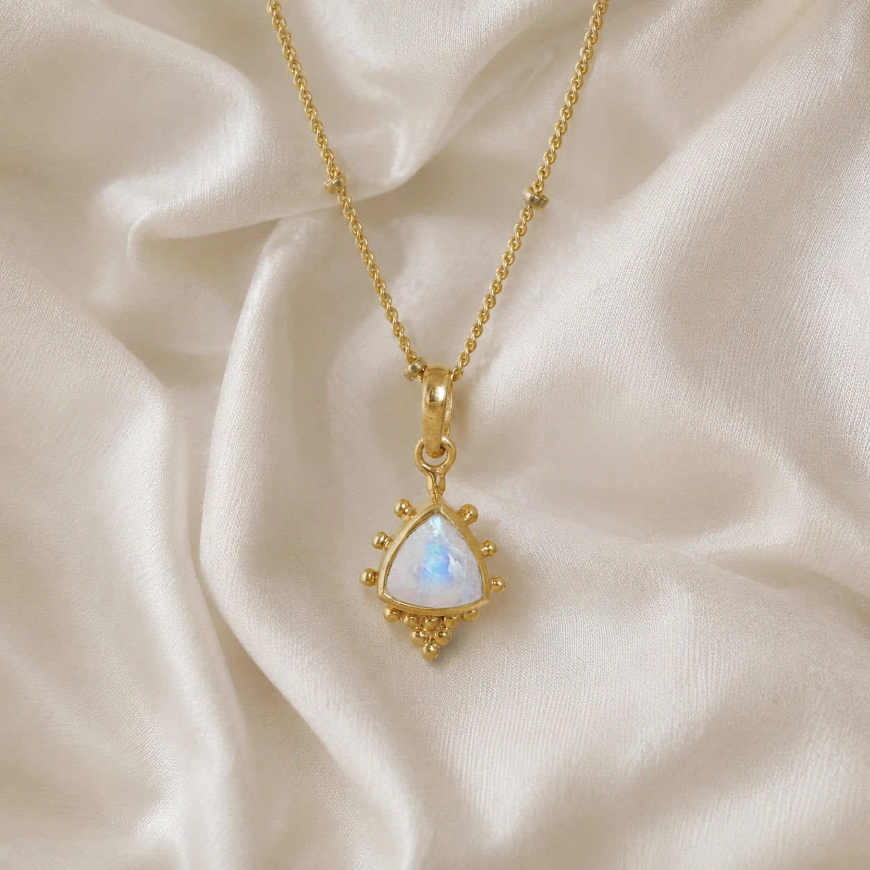 Simple_necklace_with_triangular_moonstone_pendant_gold_plated_silver_at_front_angle_on_soft_fabric_background