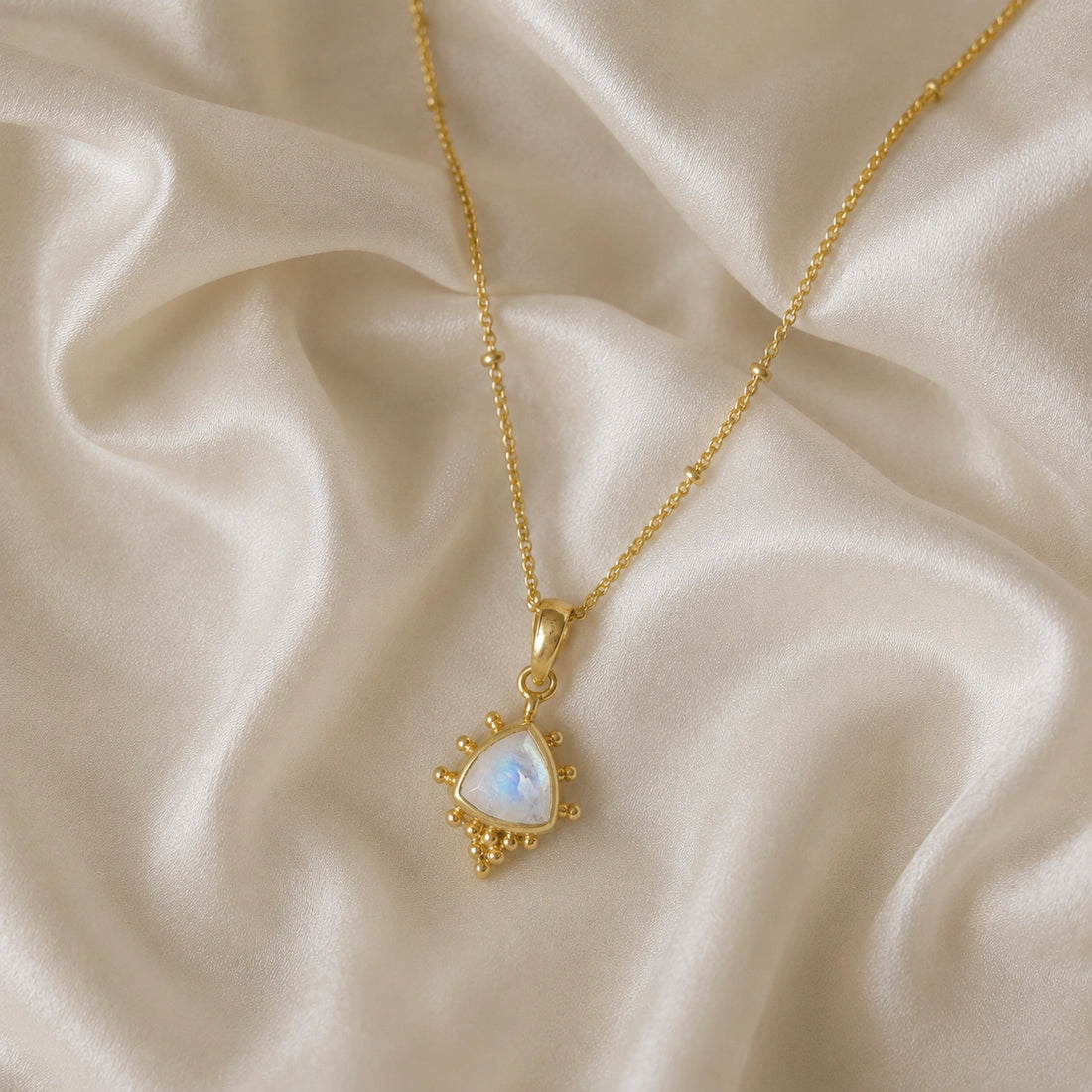 Simple_necklace_with_triangular_moonstone_pendant_gold_plated_silver_at_slightly_angled_on_soft_fabric_background
