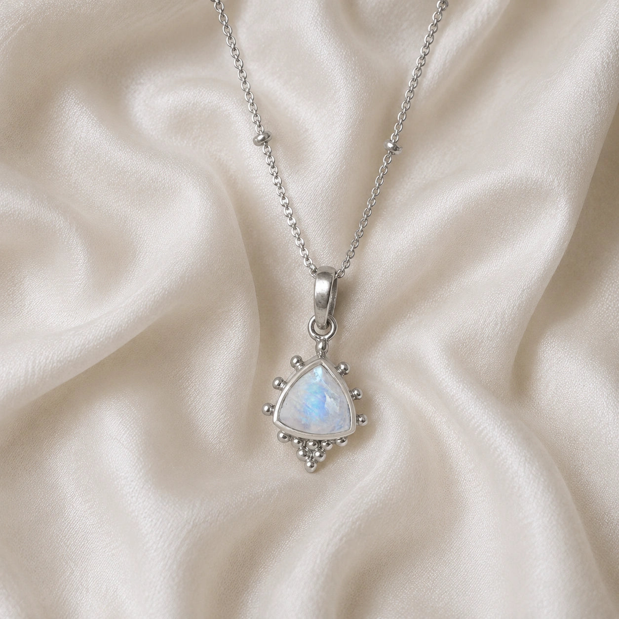 Simple_necklace_with_triangular_moonstone_pendant_sterling_silver_at_front_angle_on_soft_fabric_background