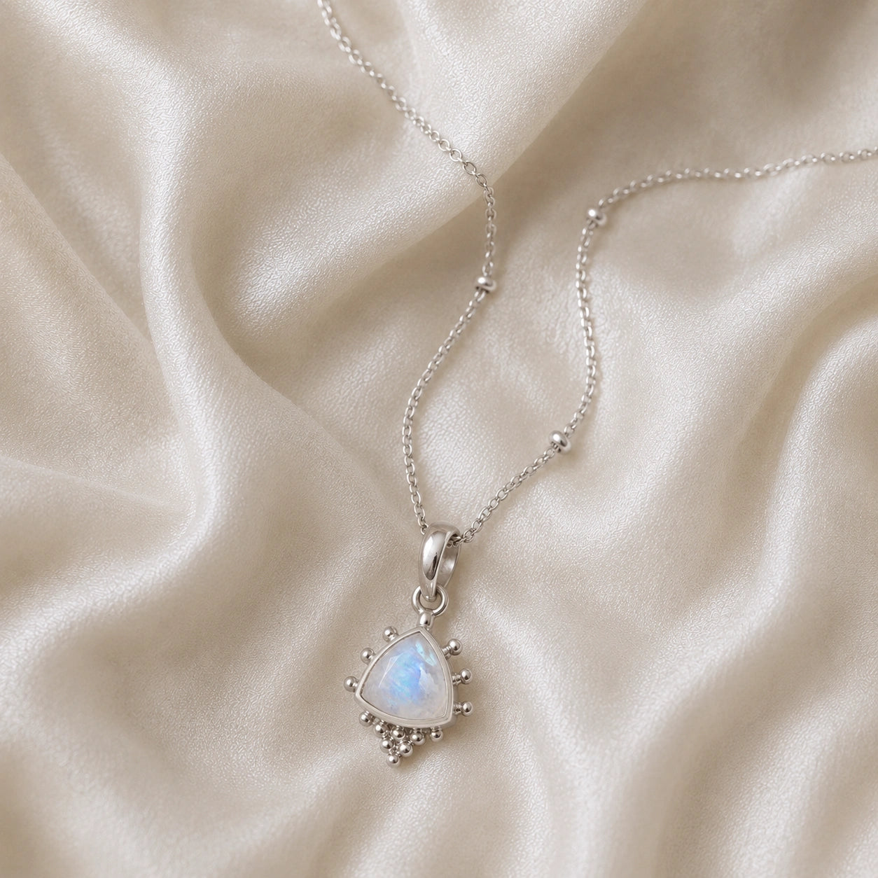 Simple_necklace_with_triangular_moonstone_pendant_sterling_silver_at_slightly_angled_on_soft_fabric_background