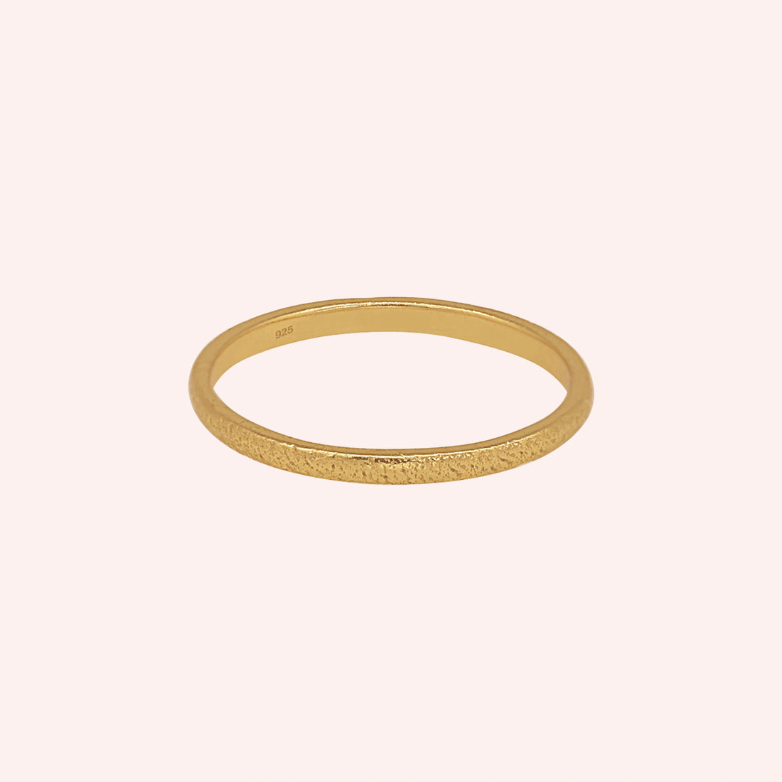Simple_ring_in_gold_plated_silver_with_a_textured_band_at_front_angle_on_solid_pink_background