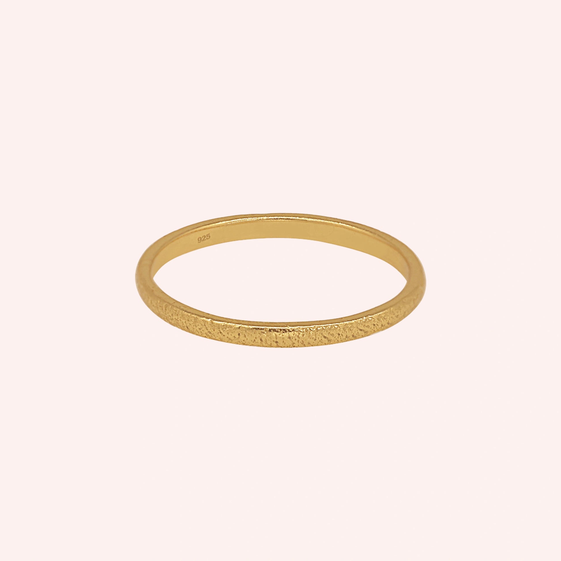 Simple_ring_in_gold_plated_silver_with_a_textured_band_at_front_angle_on_solid_pink_background