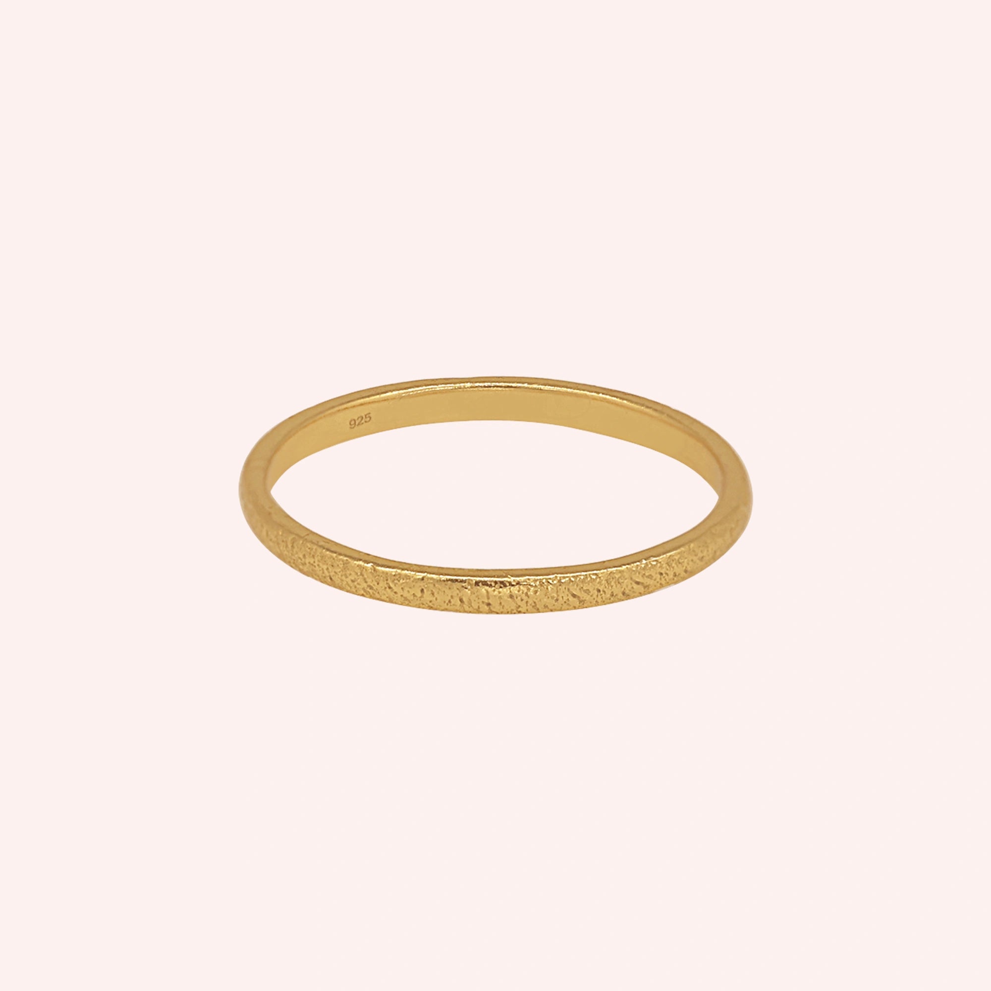 Simple_ring_in_gold_plated_silver_with_a_textured_band_at_front_angle_on_solid_pink_background