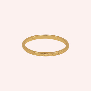 Simple_ring_in_gold_plated_silver_with_a_textured_band_at_front_angle_on_solid_pink_background