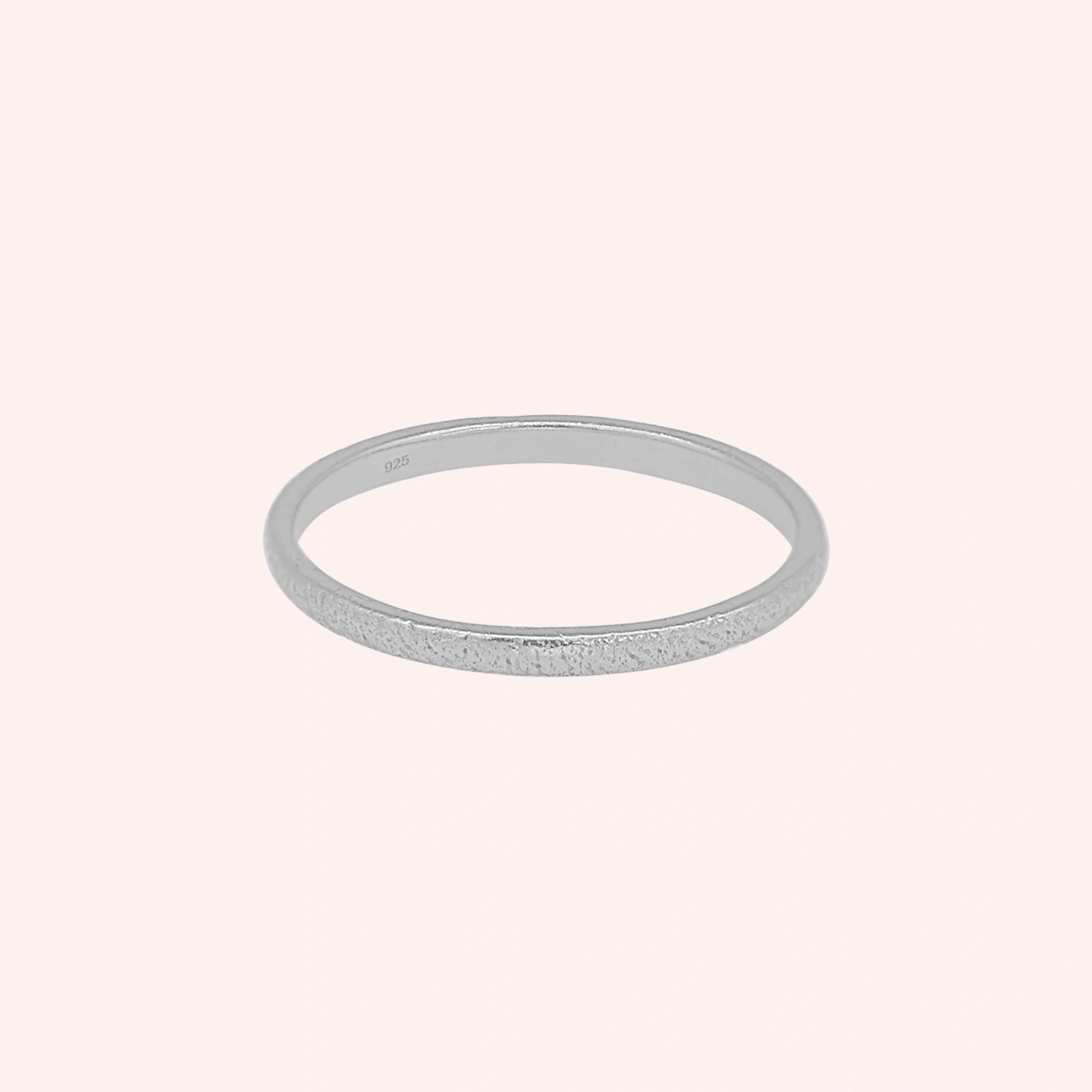 Simple_ring_in_sterling_silver_with_a_textured_band_at_front_angle_on_solid_pink_background