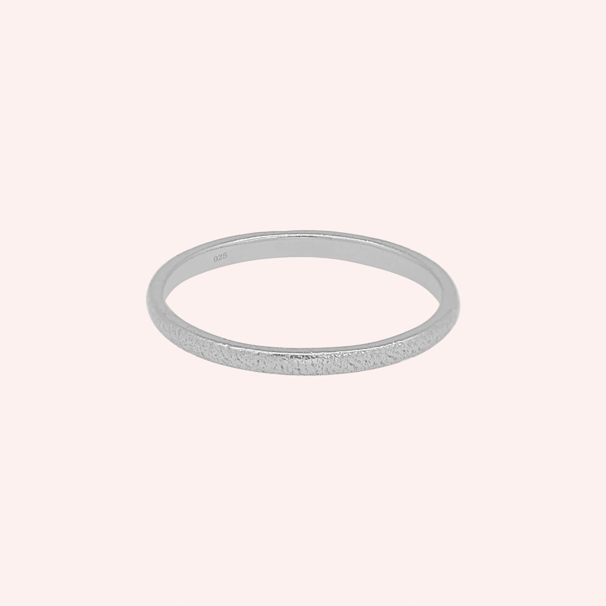 Simple_ring_in_sterling_silver_with_a_textured_band_at_front_angle_on_solid_pink_background