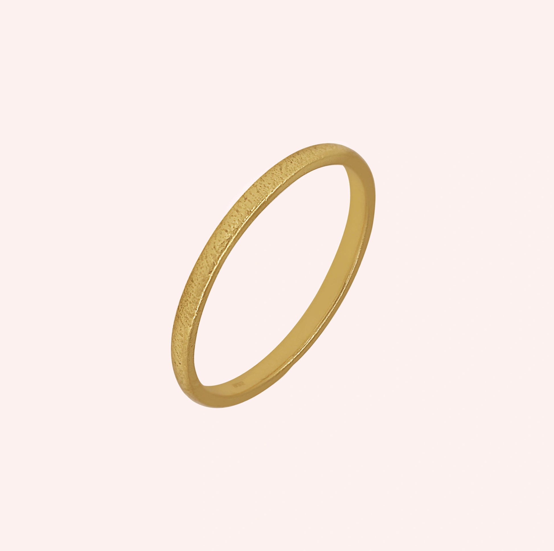 Simple_ring_in_gold_plated_silver_with_a_textured_band_at_slightly_angled_on_solid_pink_background