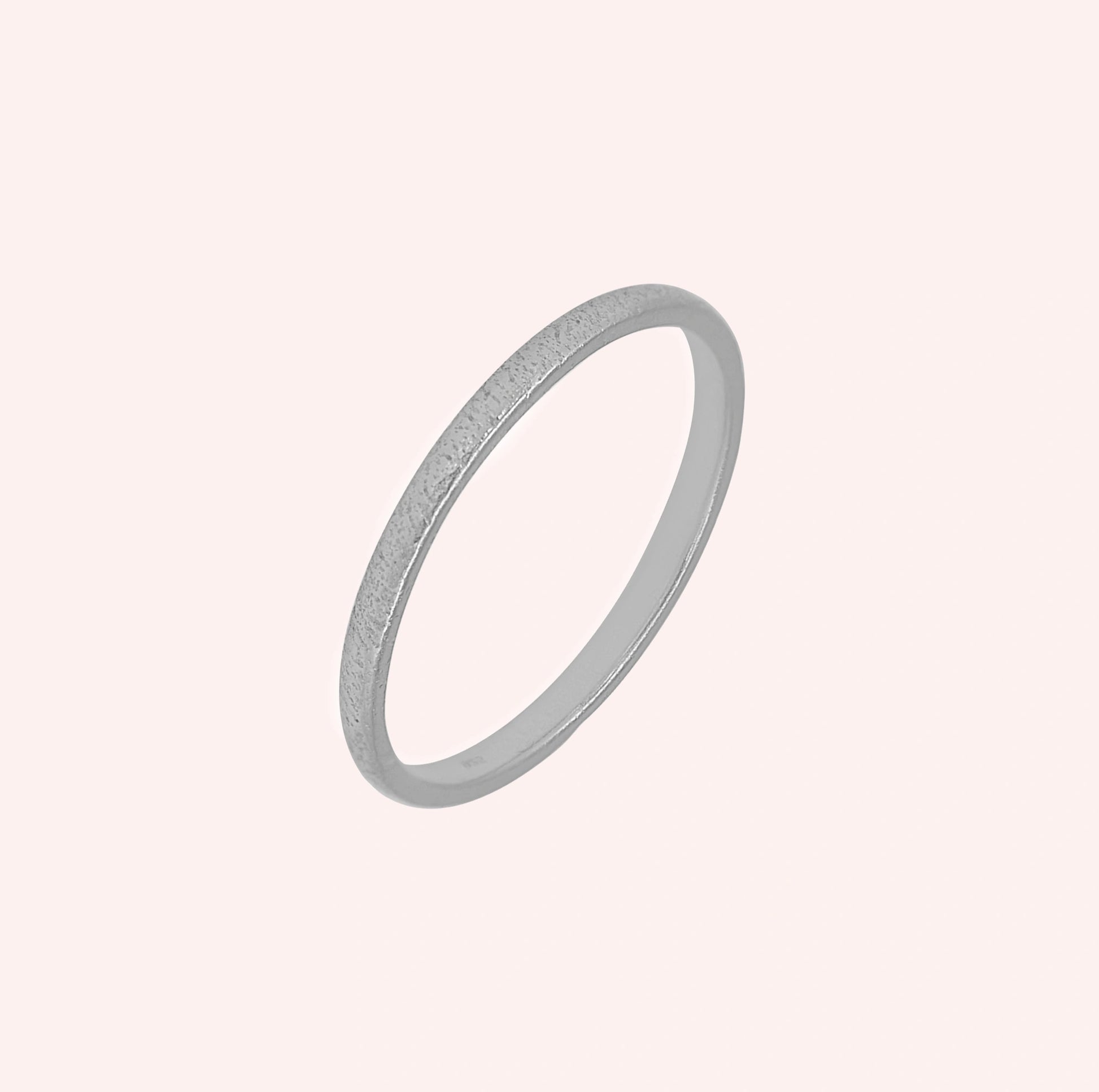 Simple_ring_in_sterling_silver_with_a_textured_band_at_slightly_angled_on_solid_pink_background
