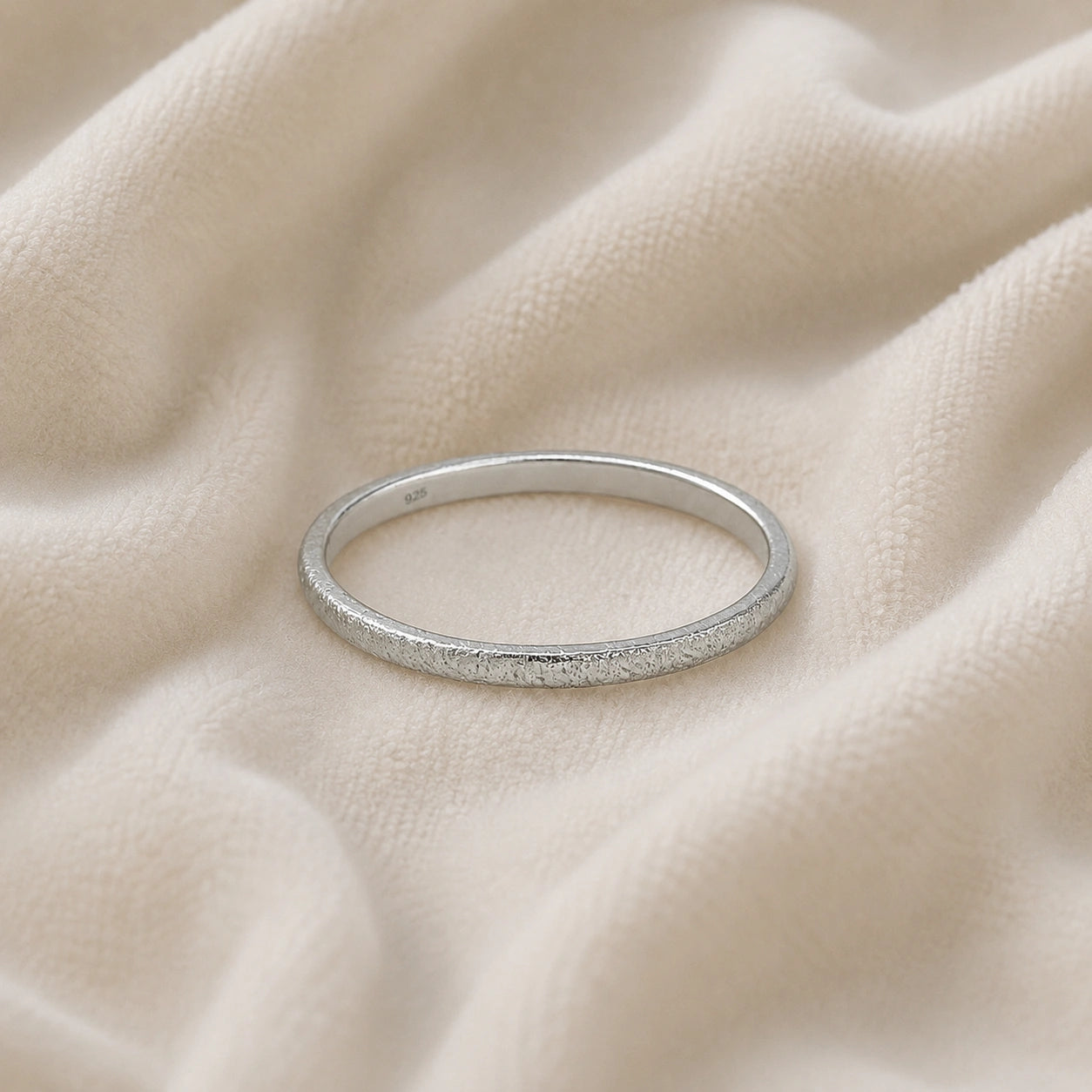 Simple_ring_in_sterling_silver_with_a_textured_band_at_front_angle_on_soft_fabric_background