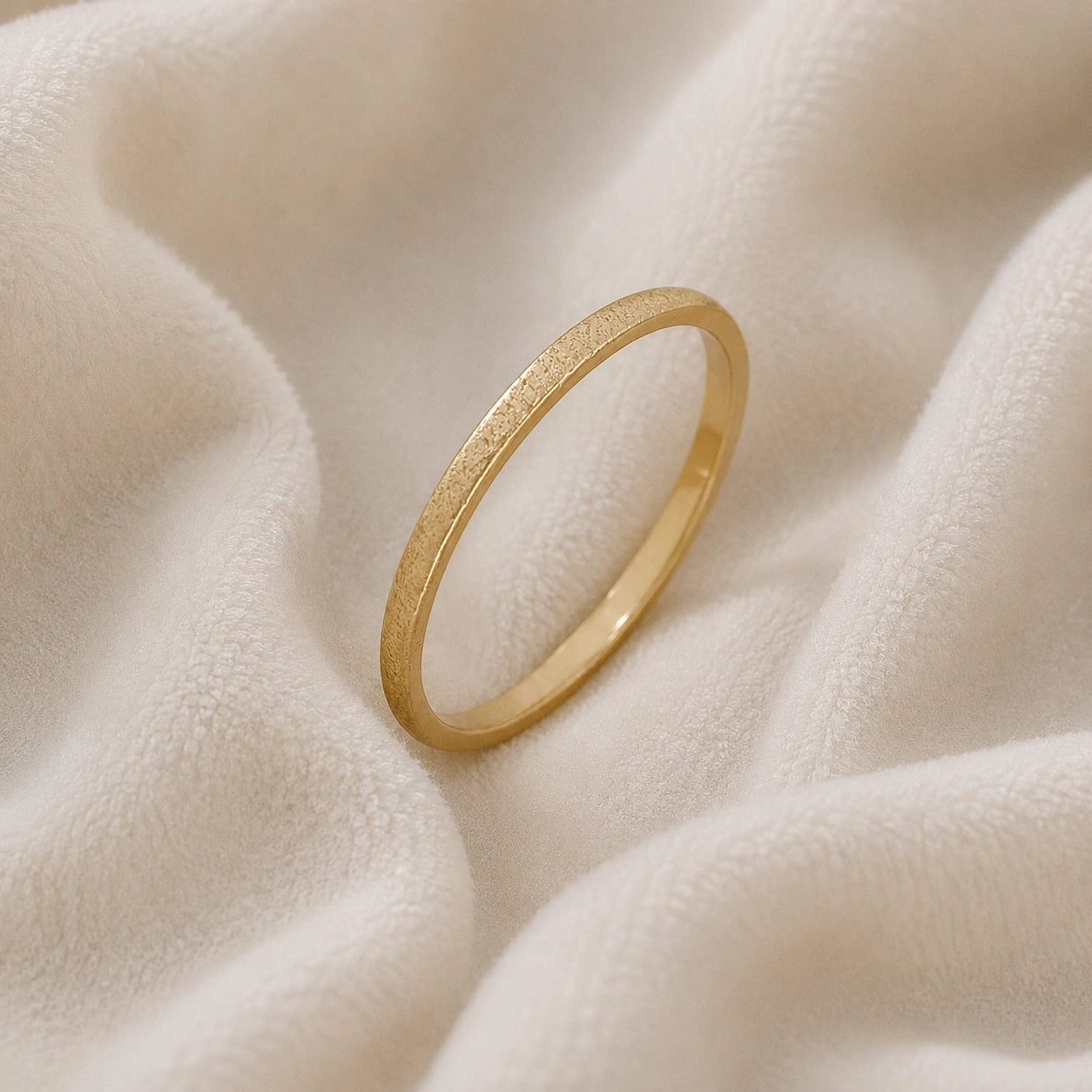 Simple_ring_in_gold_plated_silver_with_a_textured_band_at_slight_angle_on_soft_fabric_background