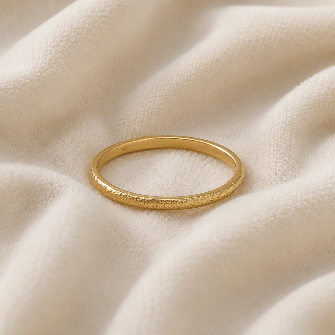 Simple_ring_in_gold_plated_silver_with_a_textured_band_at_front_angle_on_soft_fabric_background
