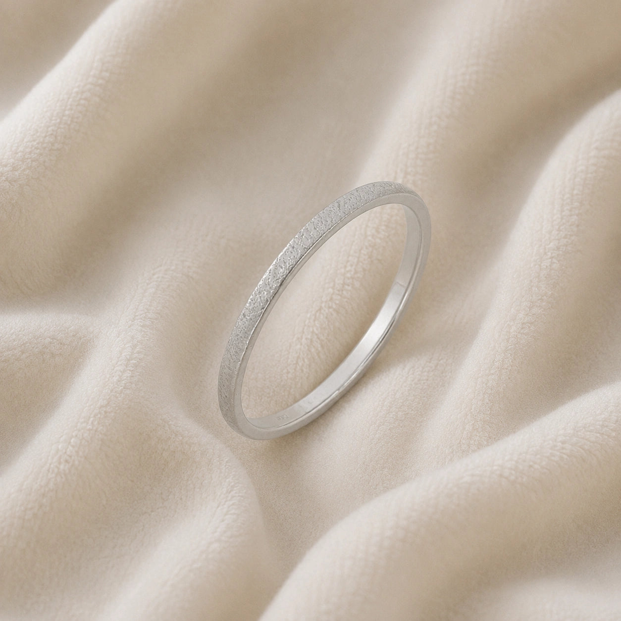 Simple_ring_in_sterling_silver_with_a_textured_band_at_slight_angle_on_soft_fabric_background
