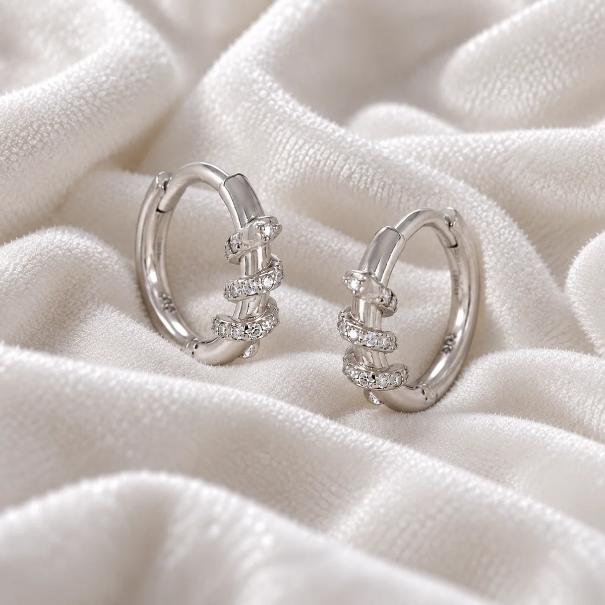 Small_hoop_earrings_in_sterling_silver_with_a_twisted_design_band_at_side_angle_view_on_soft_fabric_background