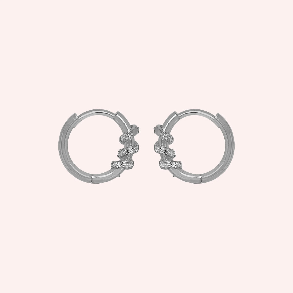 Small_hoop_earrings_in_sterling_silver_with_a_twisted_design_band_at_side_angle_view_on_solid_pink_background