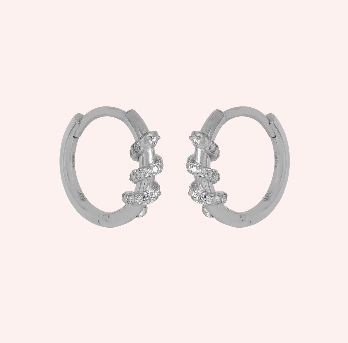 Small_hoop_earrings_in_sterling_silver_with_a_twisted_design_band_at_side_angle_view_on_solid_pink_background