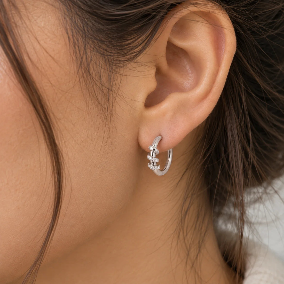Small_hoop_earrings_in_gold_plated_silver_with_a_twisted_design_band_at_side_angle_view_on_soft_fabric_background