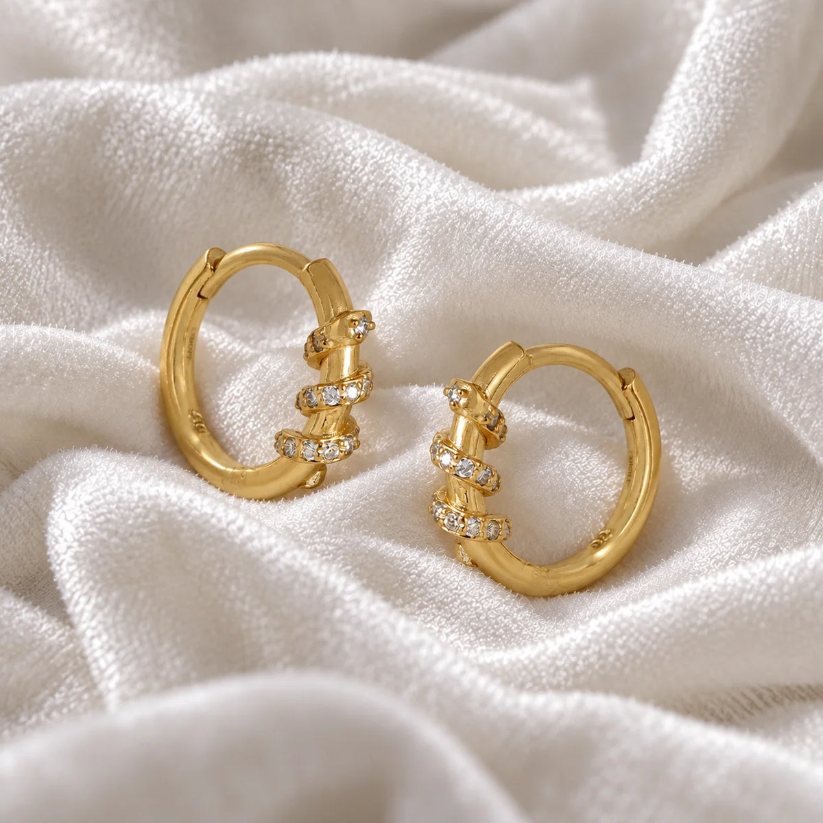 Small_hoop_earrings_in_gold_plated_silver_with_a_twisted_design_band_at_side_angle_view_on_soft_fabric_background