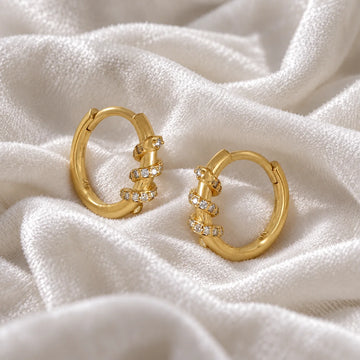 Small_hoop_earrings_in_gold_plated_silver_with_a_twisted_design_band_at_side_angle_view_on_soft_fabric_background