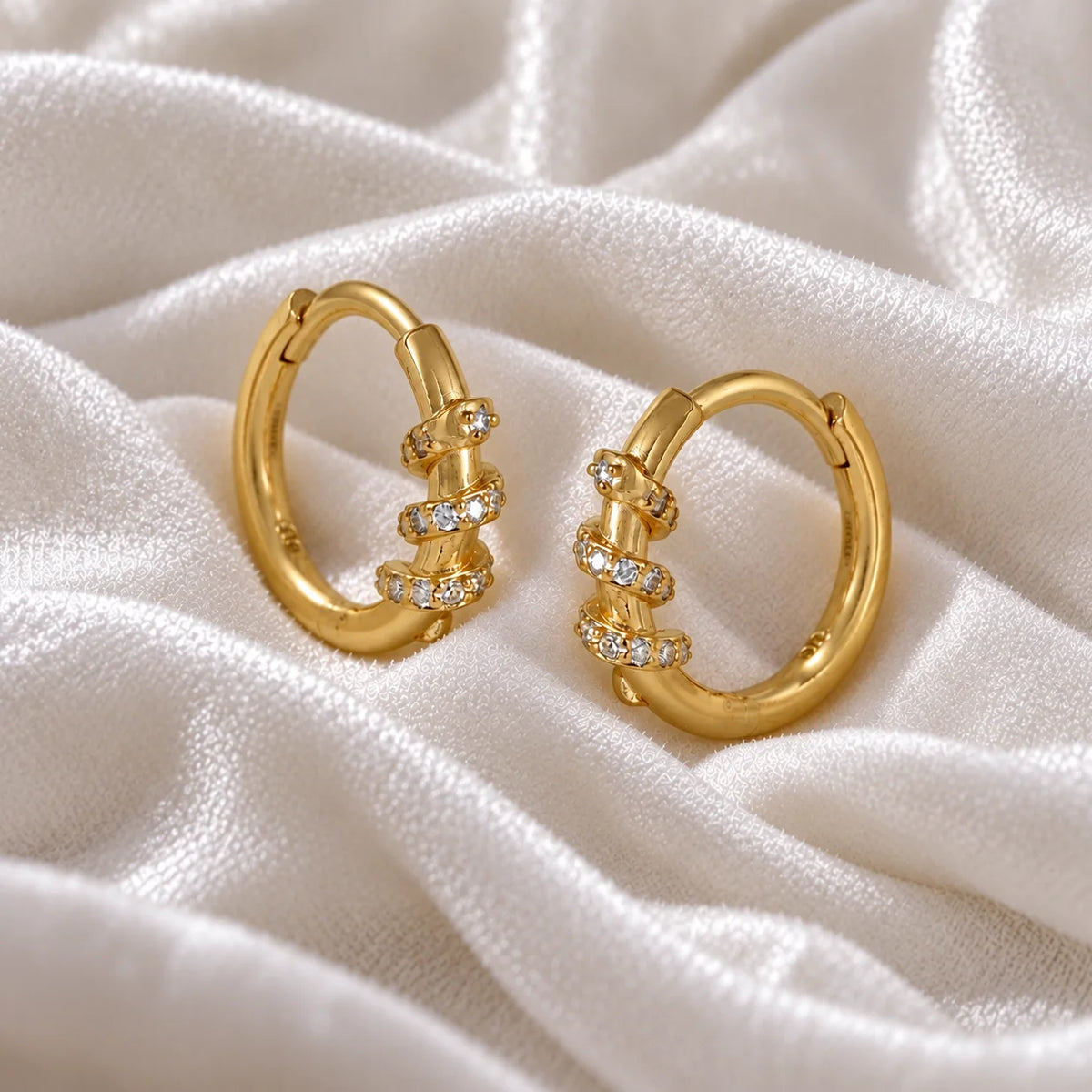 Small_hoop_earrings_in_gold_plated_silver_with_a_twisted_design_band_at_side_angle_view_on_soft_fabric_background