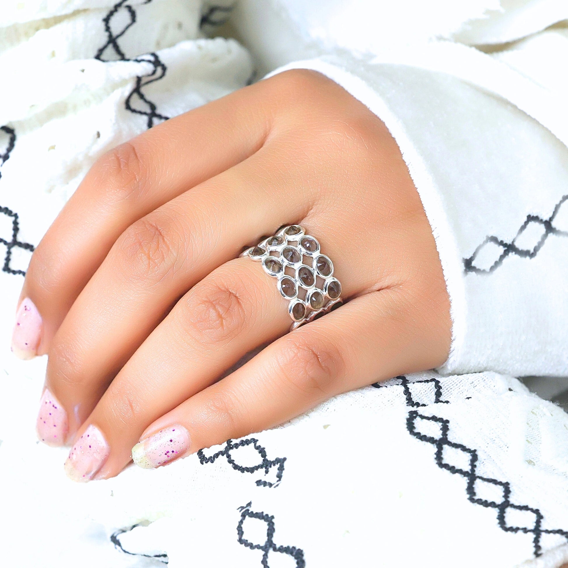 Angled close up shot of a hand wearing a wide sterling silver smoky quartz ring on a white patterned shirt background